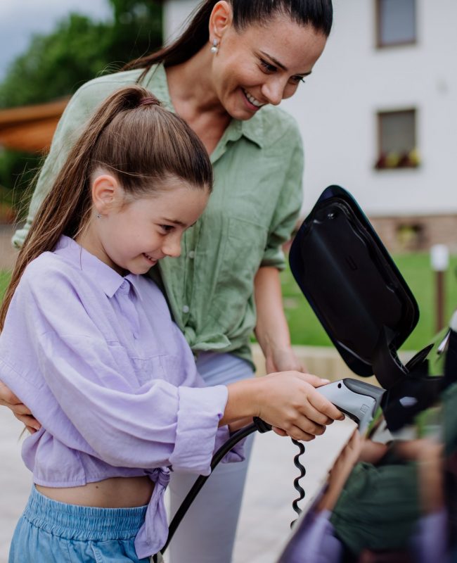 Happy mother showing her daughter how to charge their electric car.